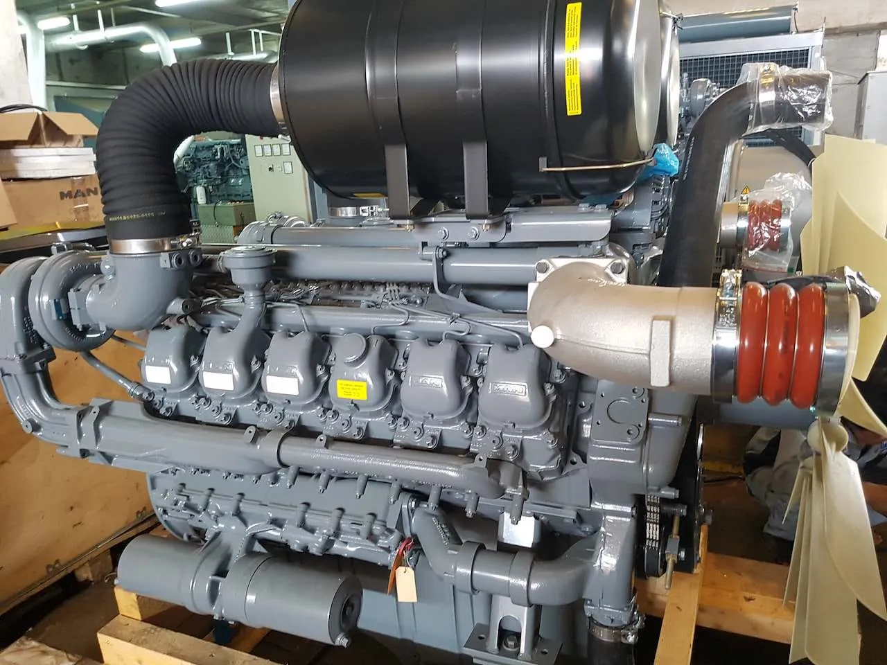 Mesin genset MAN dengan sistem turbo, exhaust, dan kipas radiator di area unboxing