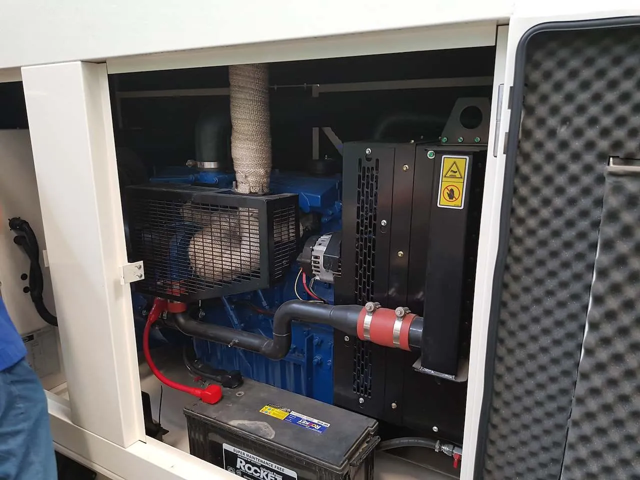 Teknisi sedang memeriksa bagian dalam genset silent type memperlihatkan mesin dan lapisan peredam suara