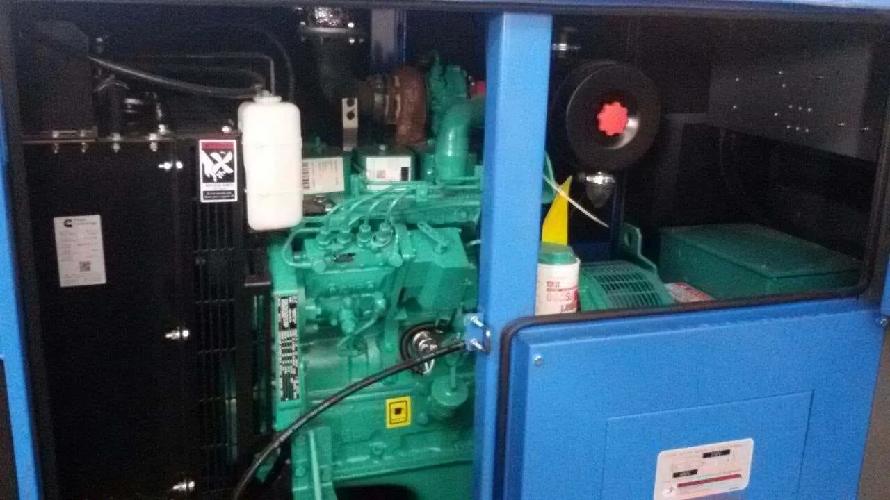 Bagian dalam genset Cummins warna hijau terlihat di dalam canopy silent type warna biru