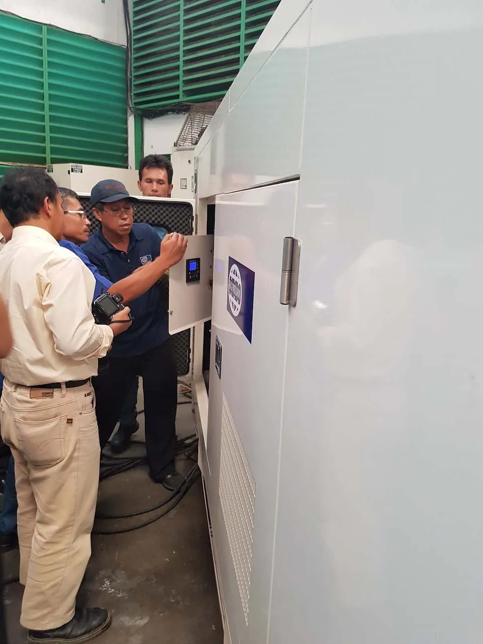Tim teknisi dan klien memeriksa panel kontrol genset FG Wilson silent type warna putih